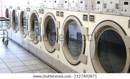 Row of washing and drying machines, public coin laundry in California, USA. Drums of washers and dryers in self-service laundromat or commercial laundrette. Automatic launderette in United States. Royalty-Free Stock Photo #2127403871