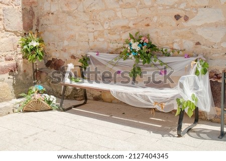 White tulle fabric adorning a bench next to a stone wall outside a church with floral decoration. Royalty-Free Stock Photo #2127404345