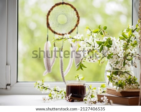 A cup of coffee on the windowsill and a branch of blooming white cherry in a vase. Spring good morning.