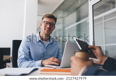 Portrait of cheerful male employee in classic eyewear for vision protection smiling at camera during working process with cropped colleague at table desktop, successful man in optical spectacles Royalty-Free Stock Photo #2127427979