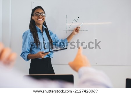 Happy mentor in optical eyewear have seminar presentation in board room training about trade exchange, half length portrait of cheerful female employee talking about diagram statistics and smiling Royalty-Free Stock Photo #2127428069