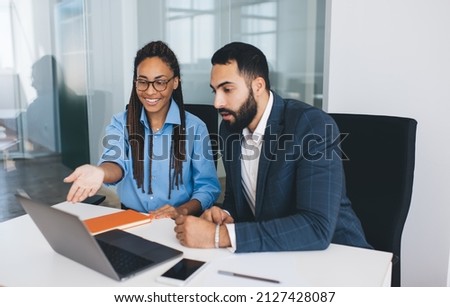 Diverse male and female colleagues watching business webinar during collaborative brainstorming at table desktop, Middle Eastern and African American employees discussing financial website Royalty-Free Stock Photo #2127428087