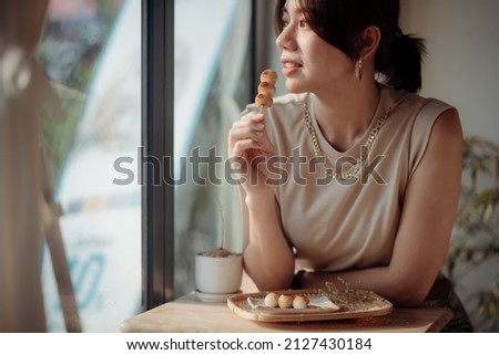 An Asian woman is tasting a Roasted Mitarashi Dango.