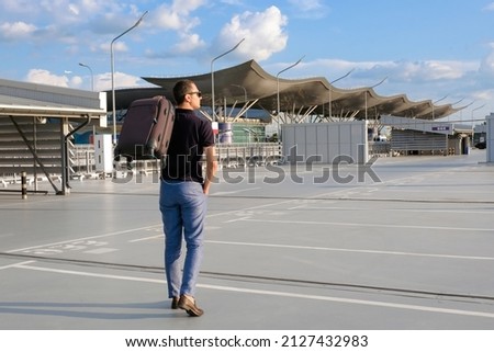 A young man with a suitcase walks in the parking lot outdoors. Business trip, vacation