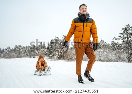 Father pulling little son on sledge in winter