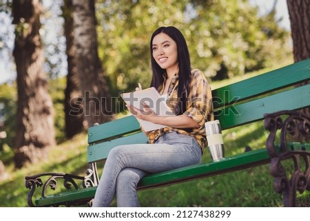 Photo of pretty cute young woman dressed plaid shirt sitting bench writing copybook smiling outside countryside nature