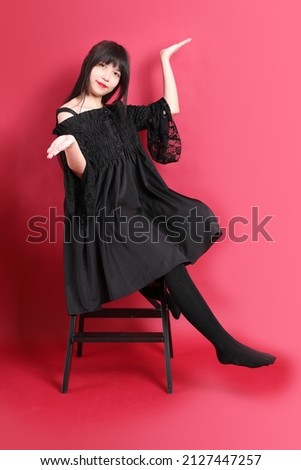 The teen Asian girl with cute gothic dressed standing on the red background.