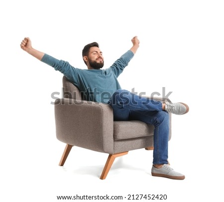 Handsome bearded man stretching in grey armchair on white background Royalty-Free Stock Photo #2127452420