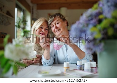Happy senior woman artist teaching her friend how to paint cermaic cup, artcraft concept. Royalty-Free Stock Photo #2127452717