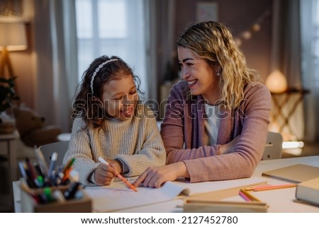 Little girl doing homework with her mother in evening at home. Royalty-Free Stock Photo #2127452780