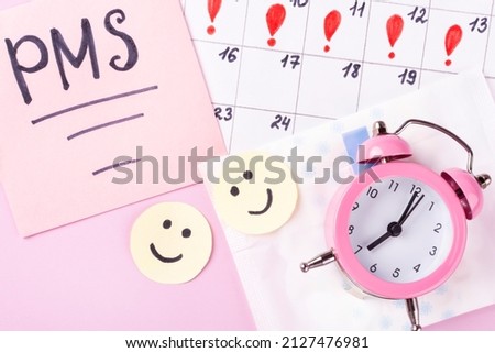 Women's Menstrual pads (sanitary napkin) in package, PMS inscription, alarm clock, menstruation calendar on a pink background. The concept of the time of critical days, women's health. Space for text. Royalty-Free Stock Photo #2127476981