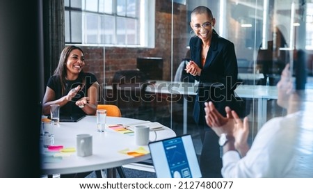 Happy young businesswoman being applauded by her colleagues during a meeting in a modern office. Successful young businesswoman smiling cheerfully while receiving praise from her colleagues. Royalty-Free Stock Photo #2127480077
