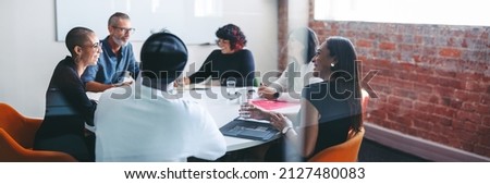 Smiling businesspeople sitting together in a meeting room. Group of successful businesspeople attending their morning briefing in a modern office. Cheerful colleagues working together. Royalty-Free Stock Photo #2127480083