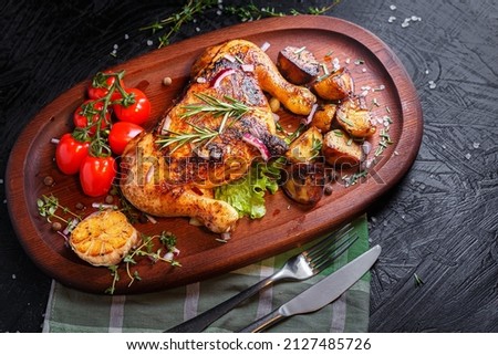 Oval wooden tray, kitchen cutting board, fried chicken, thighs with vegetables, fried potatoes, spices and vegetables, dark and moody, clouseup on a black isolated background