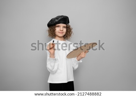 cute child girl artist poses in the studio with a paint brushe and a palette in her hands. Kid and arts. Children hobby concept.