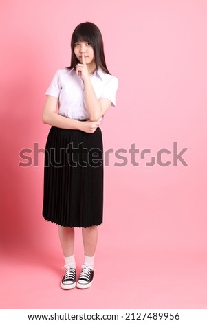 The teen Asian girl with university uniform standing on the pink background.