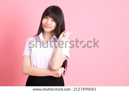 The teen Asian girl with university uniform standing on the pink background.