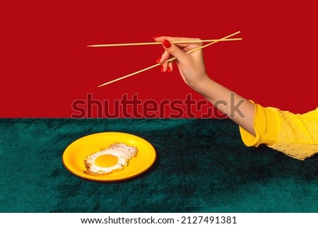 Mix cuisine. Woman's hand tasting fried eggs with chopsticks isolated on green and red background. Vintage, retro style interior. Food pop art photography. Complementary colors, Copy space for ad