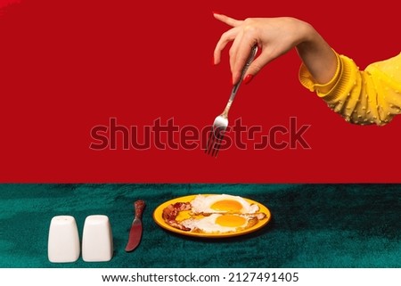 Human hand tasting bacon and eggs isolated on green and red background. Vintage, retro style interior. Food pop art photography. Complementary colors, Copy space for ad, text