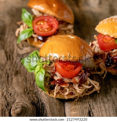 Set of homemade mini burgers with stew beef, tomatoes and basil on wooden background. Modern delicious fast food. Square image