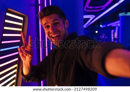 Young bristle man laughing and gesturing while taking selfie photo indoors