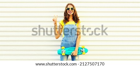 Summer portrait of happy smiling young woman posing with green skateboard on white background