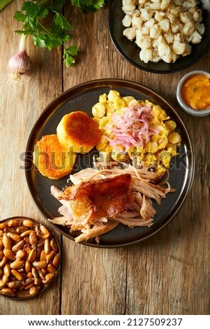 Hornado, a typical Ecuadorian dish that consists on pork cooked on firewood. It’s accompanied by llapingacho and mote pillo. Served on a black plate with a wooden background.  Royalty-Free Stock Photo #2127509237