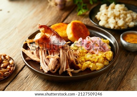 Hornado, a typical Ecuadorian dish that consists on pork cooked on firewood. It’s accompanied by llapingacho and mote pillo. Served on a black plate with a wooden background.  Royalty-Free Stock Photo #2127509246