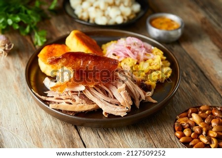Hornado, a typical Ecuadorian dish that consists on pork cooked on firewood. It’s accompanied by llapingacho and mote pillo. Served on a black plate with a wooden background.  Royalty-Free Stock Photo #2127509252