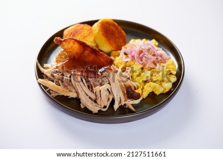 Hornado, a typical Ecuadorian dish that consists on pork cooked on firewood. It’s accompanied by llapingacho and mote pillo. Served on a black plate with a white background.  Royalty-Free Stock Photo #2127511661