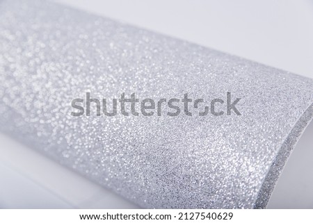 A roll of thick silver paper with glitter on a white background. Shiny fabric for creativity. Isolate