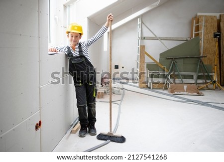 cool boy with yellow helmet posing on construction site in a house with broom
