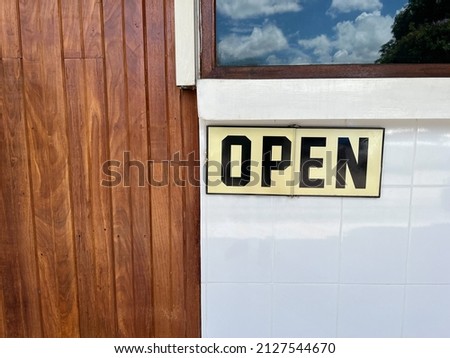 Front view with copy space of coffee shop or restaurant shows open sign on board hanging on window with beautiful reflection of sky and wooden door. It is background concept of business and commerce.