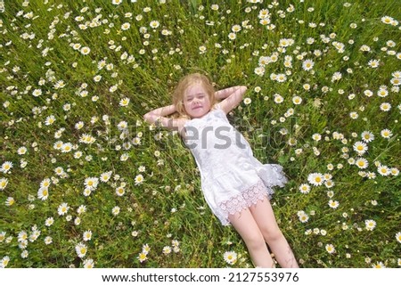 Cute little girl lie in big camomile meadow. Portrait composition.