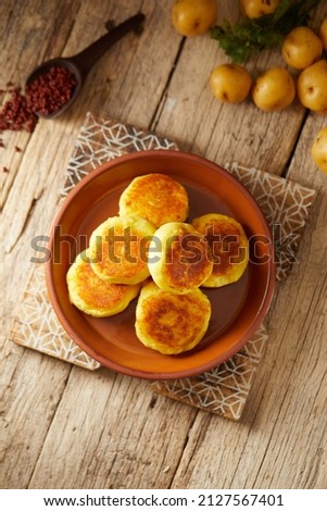 Ecuadorian llapingachos, a traditional side dish that consist on potato patties stuffed with cheese. Served on a brown plate and with a wooden and local atmosphere.  Royalty-Free Stock Photo #2127567401