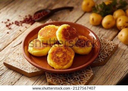 Ecuadorian llapingachos, a traditional side dish that consist on potato patties stuffed with cheese. Served on a brown plate and with a wooden and local atmosphere.  Royalty-Free Stock Photo #2127567407