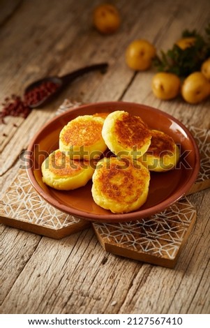 Ecuadorian llapingachos, a traditional side dish that consist on potato patties stuffed with cheese. Served on a brown plate and with a wooden and local atmosphere.  Royalty-Free Stock Photo #2127567410
