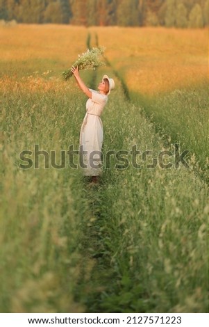 a beautiful woman in a simple linen dress in a field with a bouquet of wildflowers in her hands at sunset, the concept of summer walks, folklore simple style.
