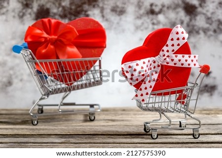 Two shopping carts with gift boxes in heart shape on a rustic wooden table. Sales and shopping concept.