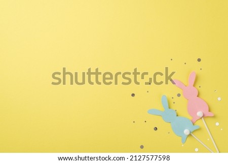 Top view of two rabbits pink and blue one with confetti on the isolated yellow background copyspace