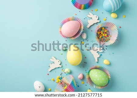 Top view photo of easter decor composition funny easter bunnies multicolored easter eggs in paper baking molds and confectionery topping on isolated pastel blue background with blank space