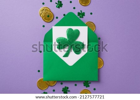 Top view photo of green envelope with white card inside and nice shamrock on it golden coins confetti in shape of clovers and dots in the middle of isolated violet background copyspace