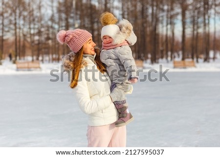 a beautiful slender woman lifts a two-year-old girl. people in winter in outerwear