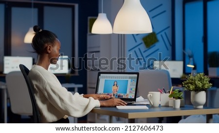 Dark skin freelancer retoucher woman working overtime on laptop with photo editing software. Professional graphic editor retouching photo of a client during night time in home office on performance pc