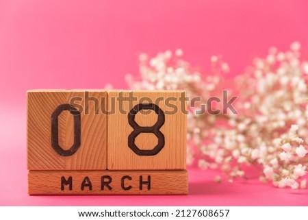 International Women's Day. Beautiful postcard for March 8. A bouquet of tender gypsophila and a wooden calendar on a pink paper background. Holiday concept. Copy space. Side view.