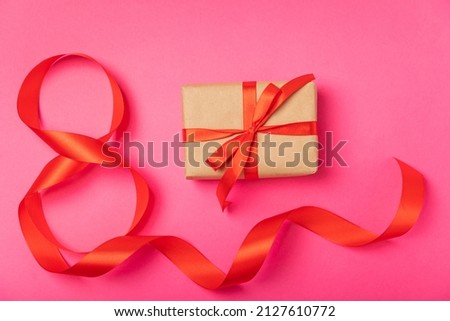 March 8, International Women's Day. Number eight from a red ribbon and a gift box with a satin ribbon on a pink paper background. Place for text