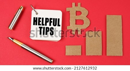 Business and bitcoin concept. On a red surface lie a bitcoin symbol, a graph, a pen and a notepad with the inscription - Helpful Tips