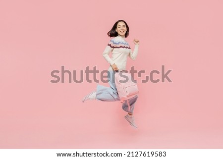 Full body happy excited teen student girl of Asian ethnicity in sweater hold backpack jump high do winner gesture isolated on pastel plain light pink background Education in university college concept