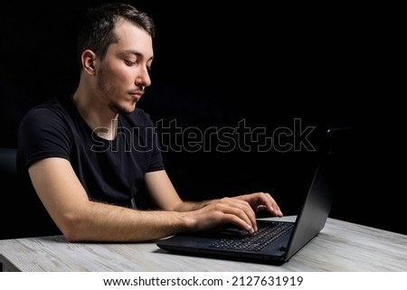 Young male writer with laptop on black background in low or dark key. Background