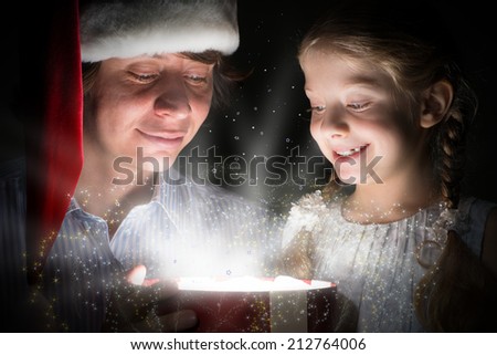 father in Santa Claus cap and daughter opened a box with Christmas gift boxes of shining light and magic